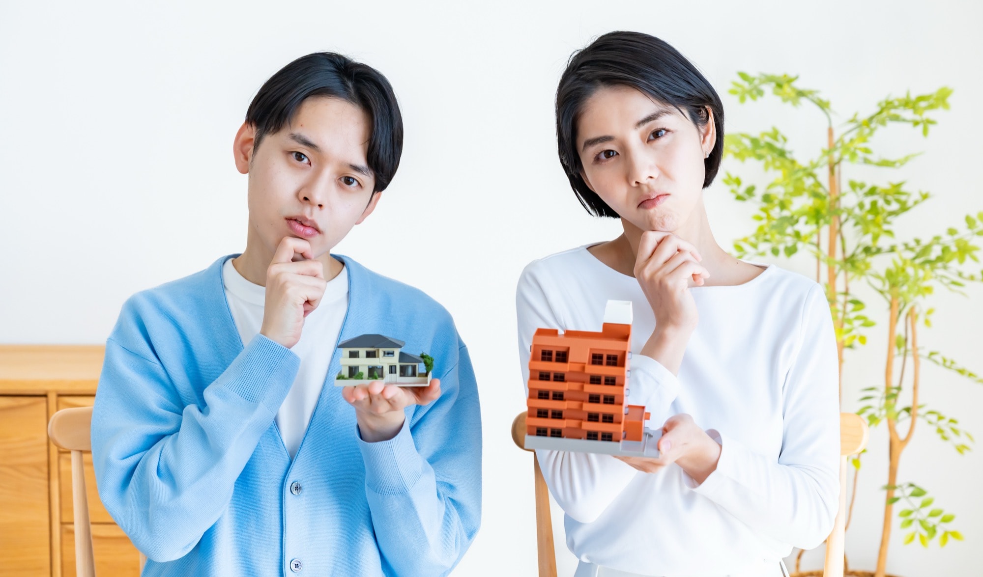 マンションと戸建て住宅の模型を持って考える男女